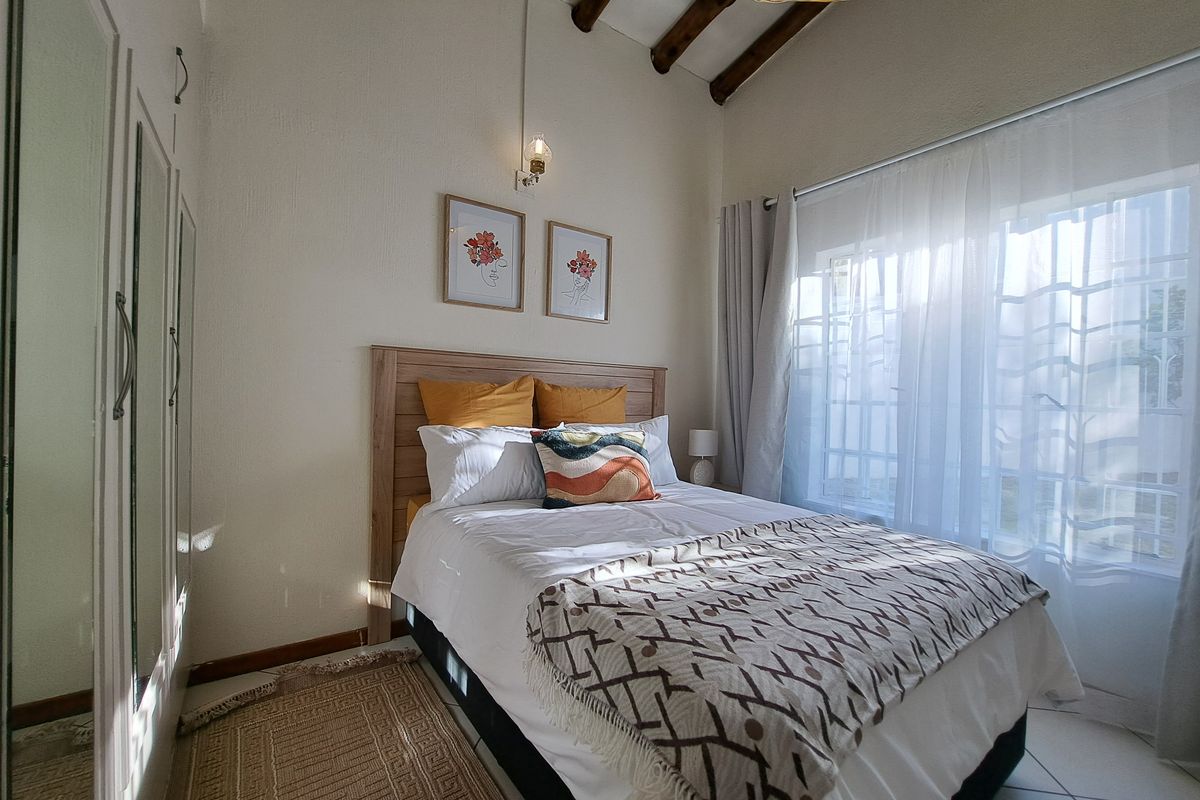 A cozy bedroom featuring exposed timber ceiling beams, tiled flooring, and a built-in wardrobe with mirrored doors, offering a bright and inviting atmosphere.