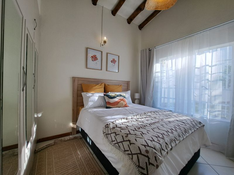 A cozy bedroom featuring exposed timber ceiling beams, tiled flooring, and a built-in wardrobe with mirrored doors, offering a bright and inviting atmosphere.