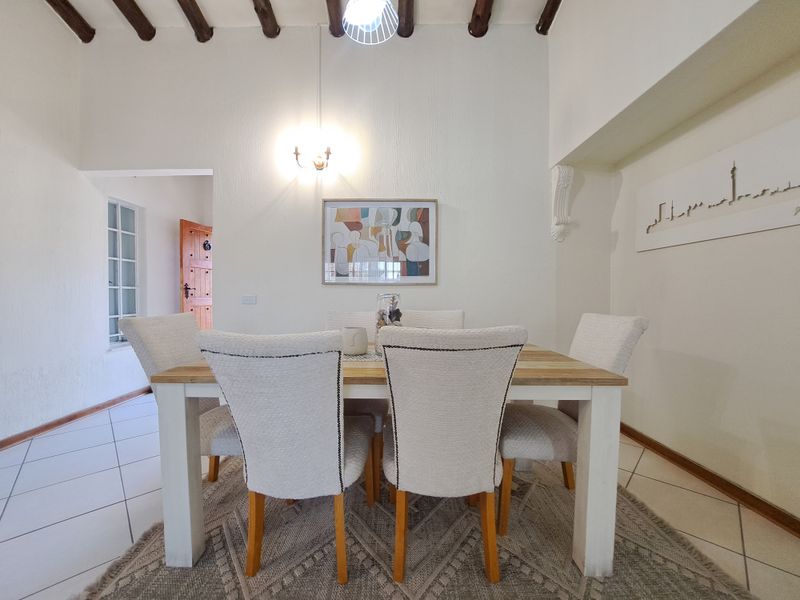A bright dining room featuring exposed timber ceiling beams, tiled flooring, and classic wall sconce lighting, creating a warm and inviting atmosphere.