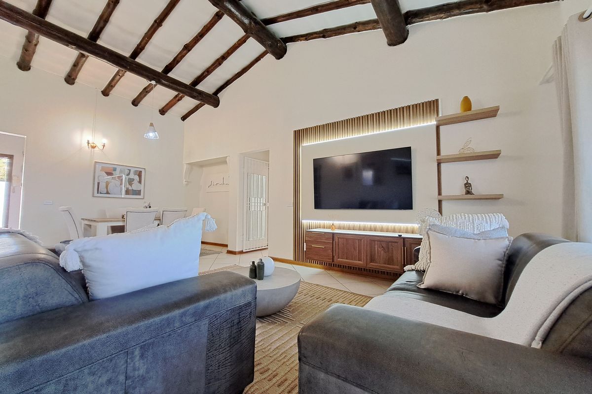 Spacious open-plan living area featuring a vaulted ceiling with exposed timber beams, tiled flooring, and a modern built-in media unit with integrated lighting.