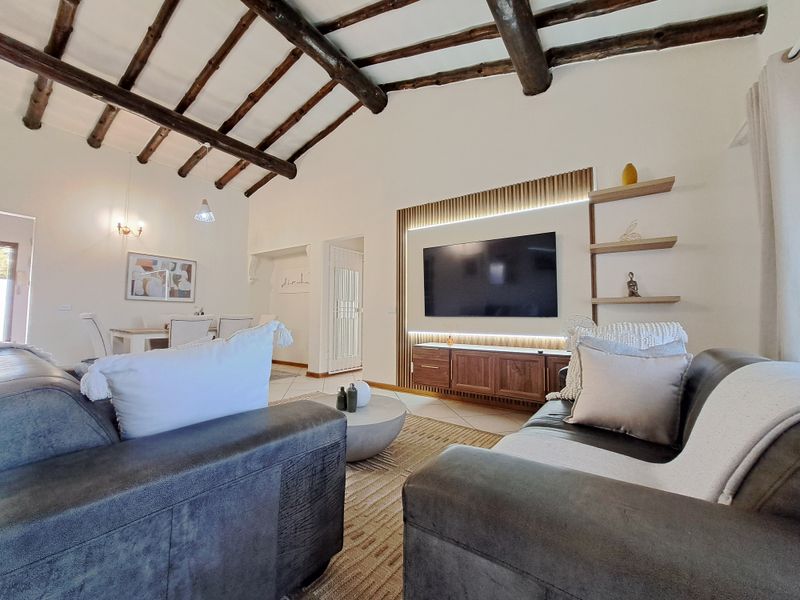 Spacious open-plan living area featuring a vaulted ceiling with exposed timber beams, tiled flooring, and a modern built-in media unit with integrated lighting.