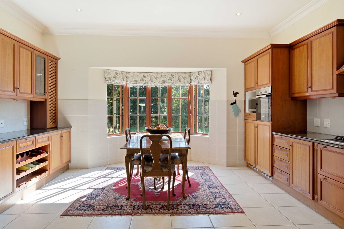 Spacious kitchen featuring timber cabinetry, built-in oven, tiled flooring, and a bright bay window overlooking the garden.