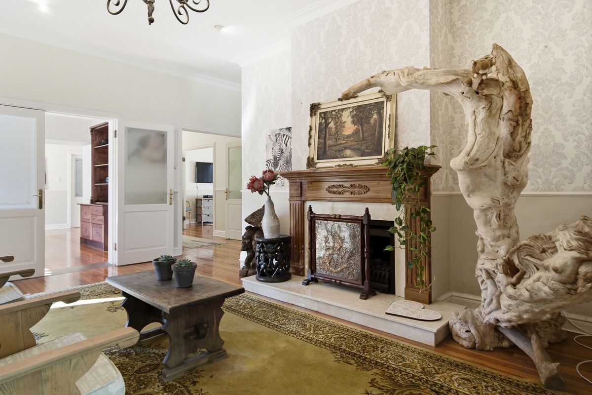 A well-maintained living room featuring a classic wooden fireplace mantel with a marble hearth, hardwood flooring, and elegant double door access to adjacent rooms.
