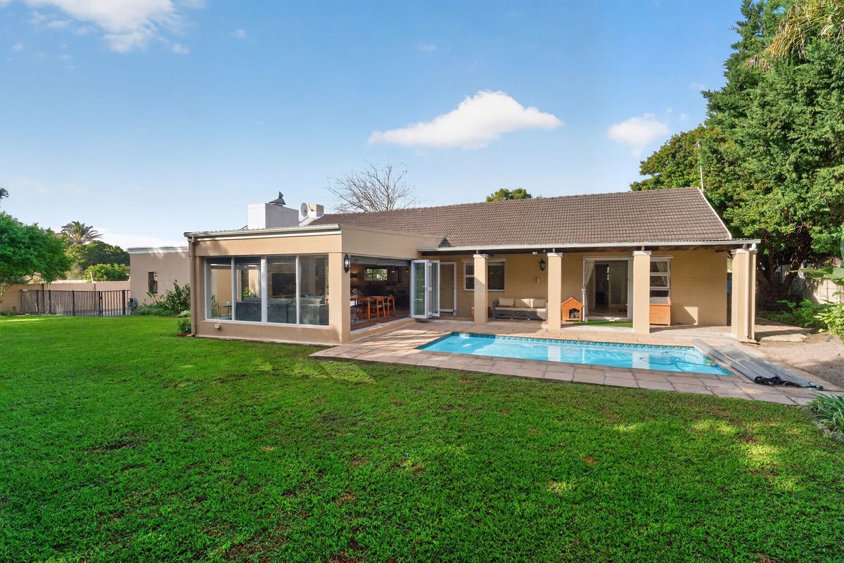 Rear view of the property featuring a swimming pool, covered patio area, and bi-fold doors leading into the living space.