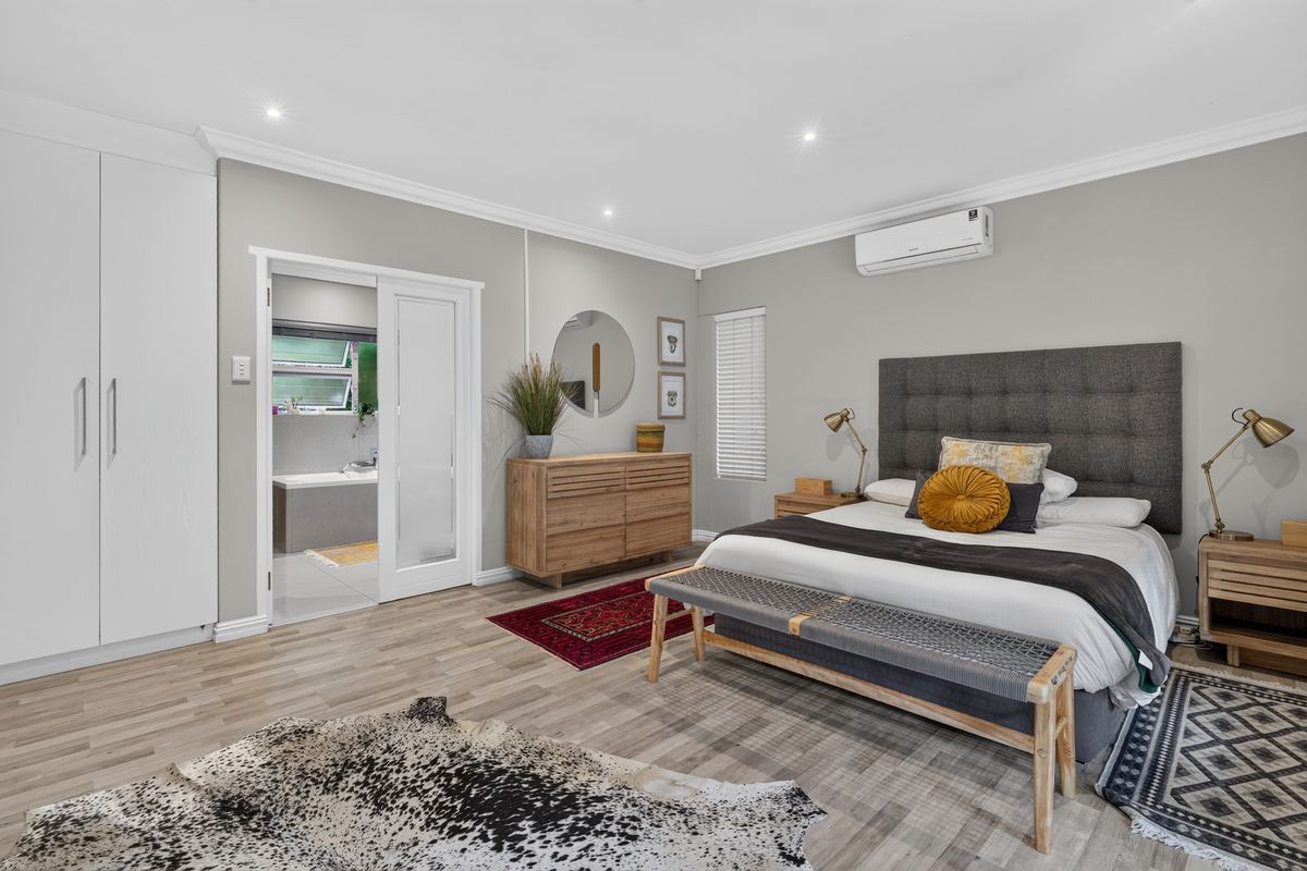 Spacious bedroom featuring laminate flooring, built-in wardrobes, recessed lighting, and an en-suite bathroom accessible via a sliding door.