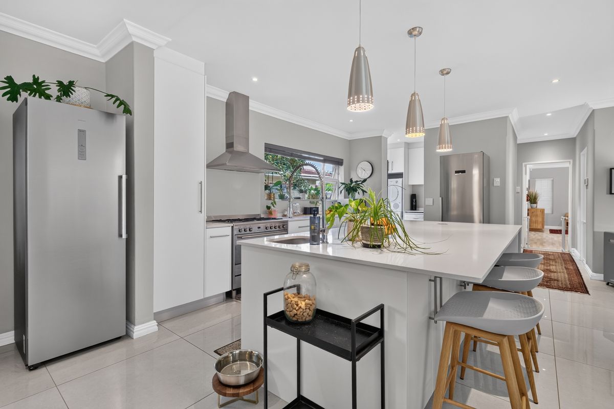 Modern kitchen featuring a large central island with quartz countertops, stainless steel appliances, sleek white cabinetry, and elegant pendant lighting.
