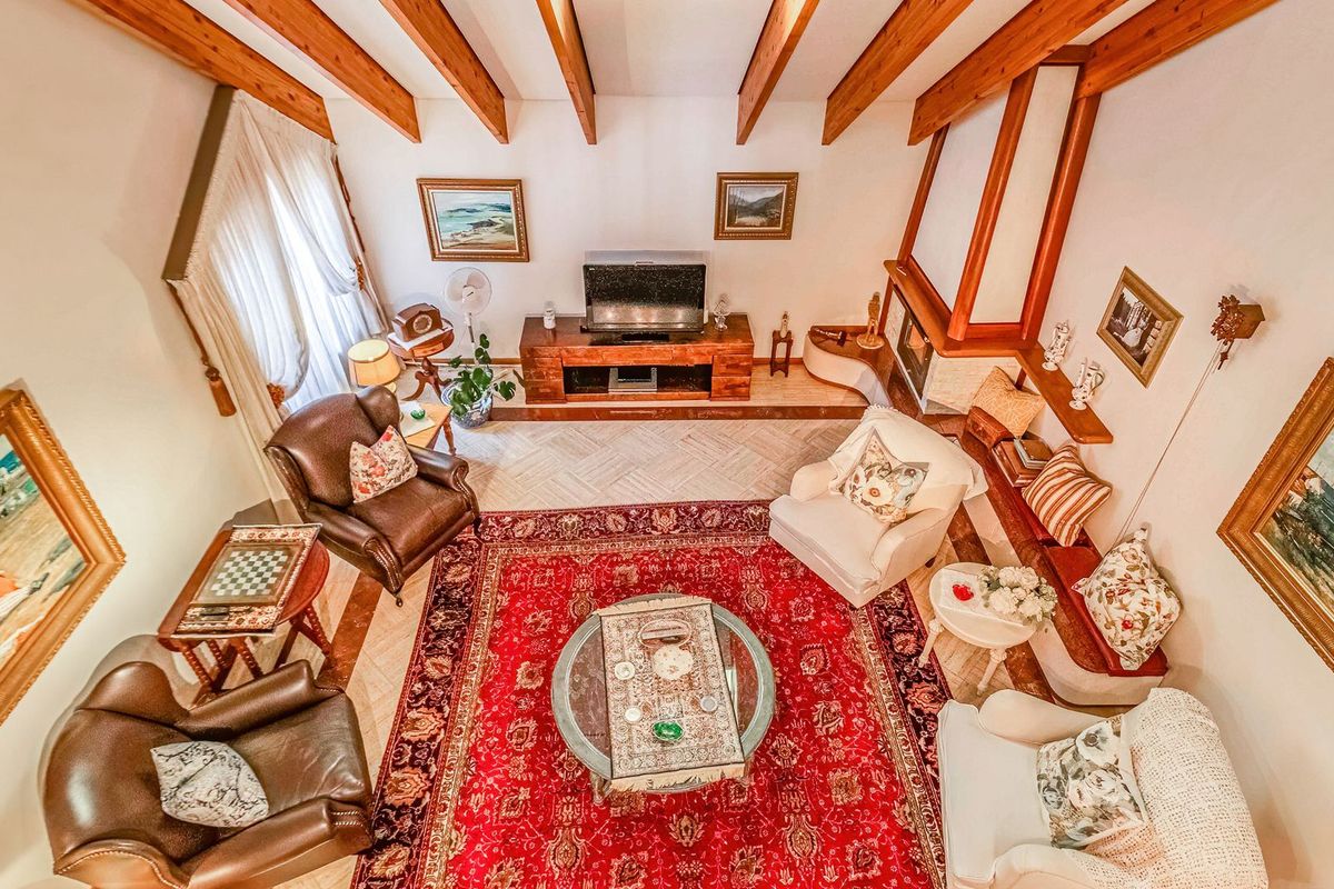 Spacious living room featuring high vaulted ceilings with exposed timber beams, a built-in fireplace, and elegant herringbone flooring.