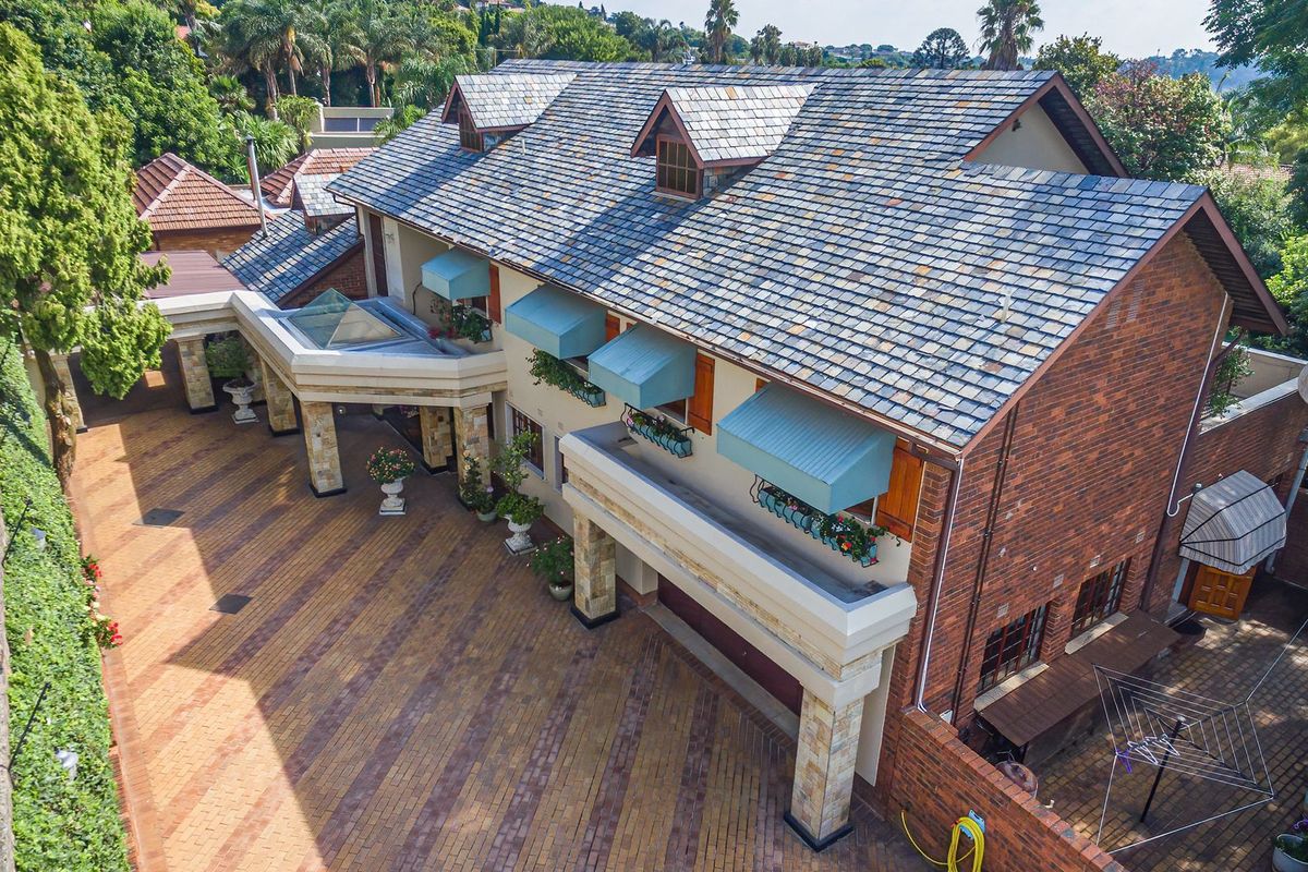 Aerial view of a large multi-story residence featuring a slate roof, brick exterior, stone-clad entrance pillars, and an expansive paved driveway.
