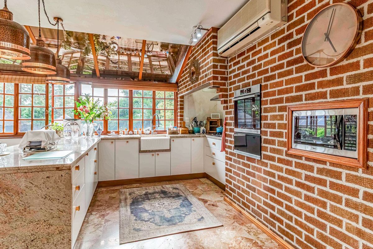 A character-filled kitchen featuring exposed brick walls, granite countertops, an apron sink, and a unique glass-paneled roof that provides abundant natural light.