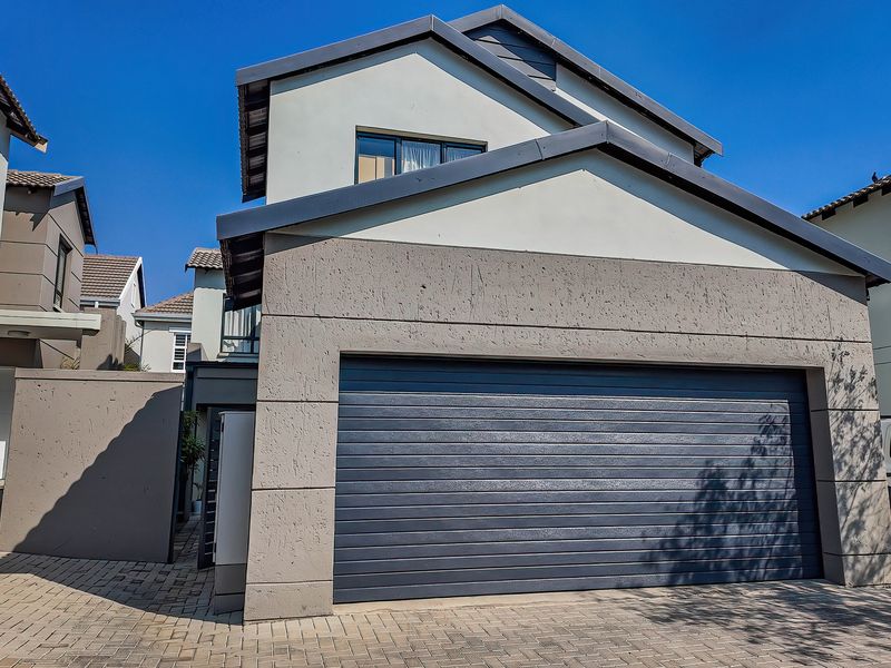 Front elevation of a modern townhouse featuring a double garage, textured plaster facade, and a paved driveway.