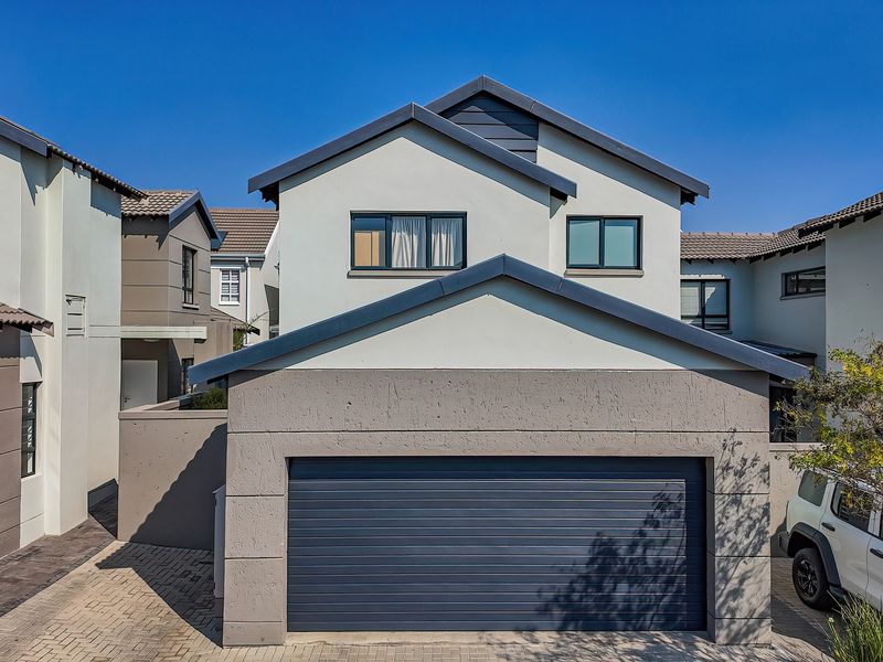 Front elevation of a modern townhouse featuring a double garage, paved driveway, and contemporary architectural finishes with a tiled roof.