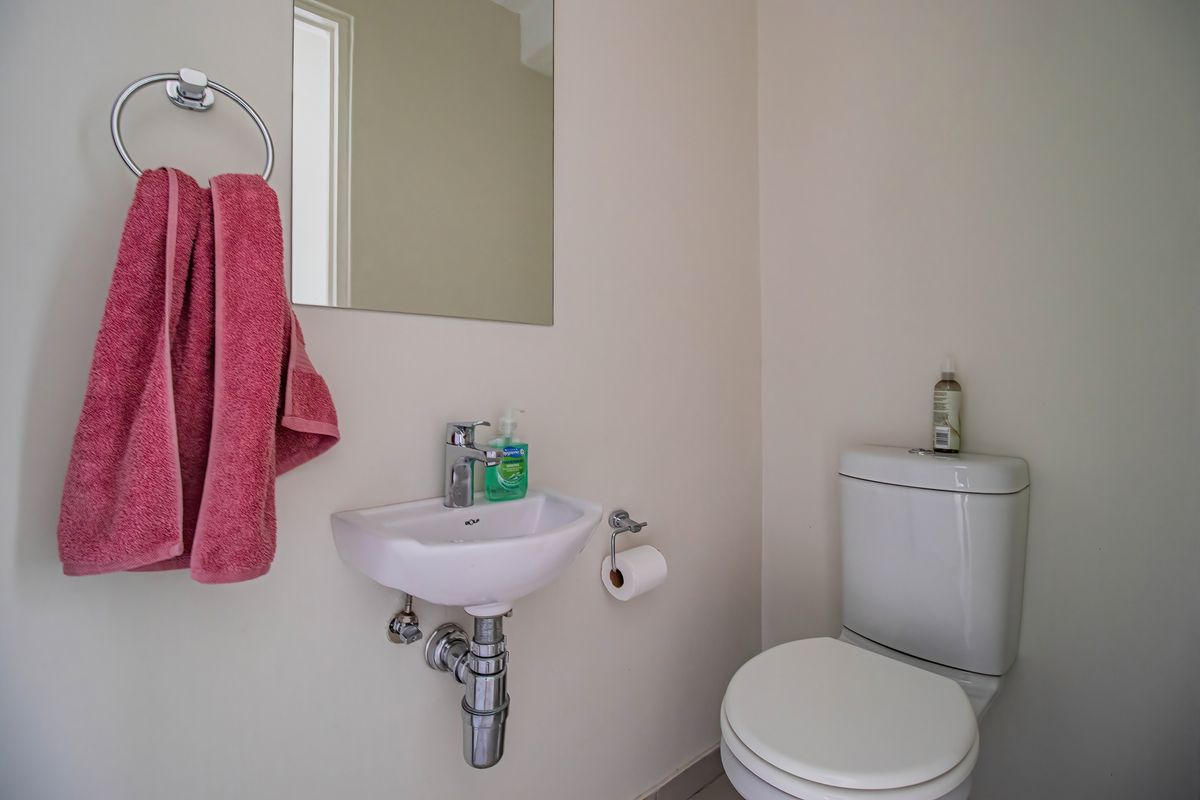 A compact guest bathroom featuring a wall-mounted basin, chrome fixtures, and a standard toilet, finished with neutral wall tones.