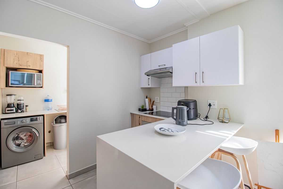 Modern kitchen featuring white cabinetry, stone countertops, a breakfast bar, and a subway tile backsplash, with an adjacent laundry area.