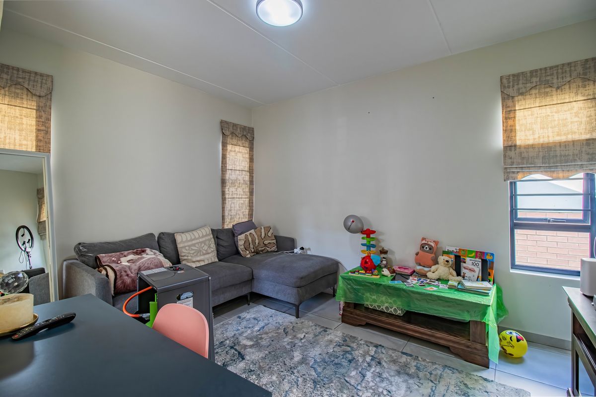 A living room featuring tiled flooring, neutral walls, and multiple windows with fitted blinds, providing a functional and well-lit living space.