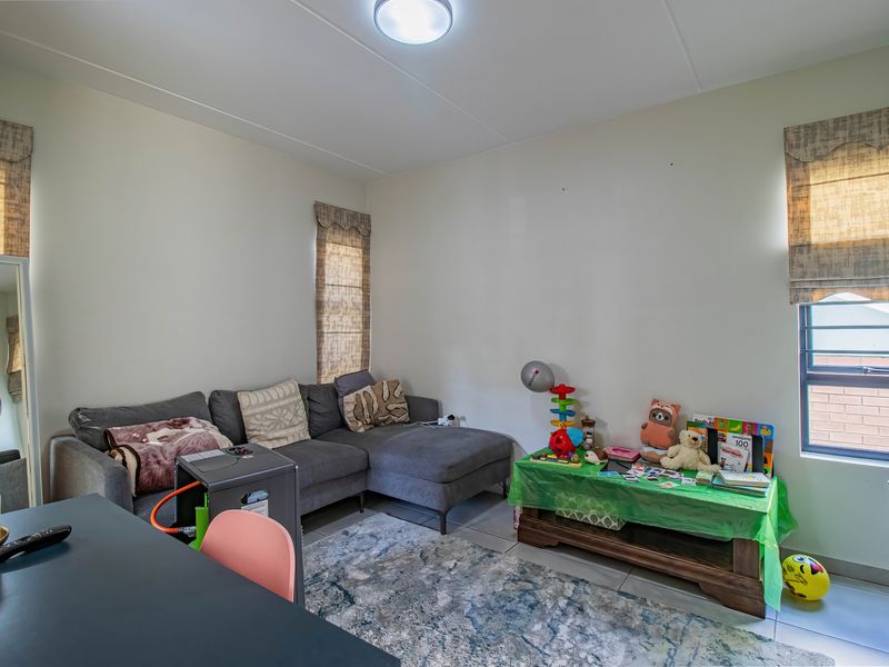 A living room featuring tiled flooring, neutral walls, and multiple windows with fitted blinds, providing a functional and well-lit living space.