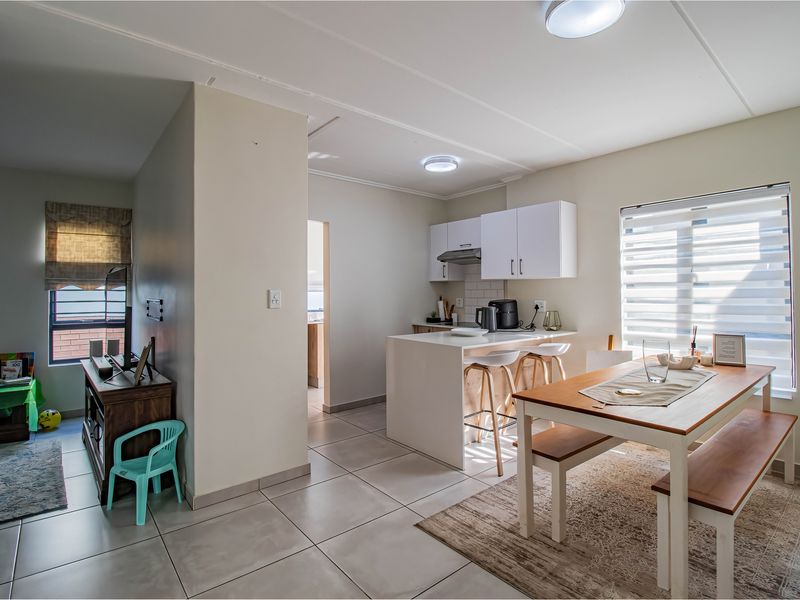 Open-plan living and dining area featuring tiled floors, a modern kitchen with built-in cabinetry, an island, and natural light through roller blinds.