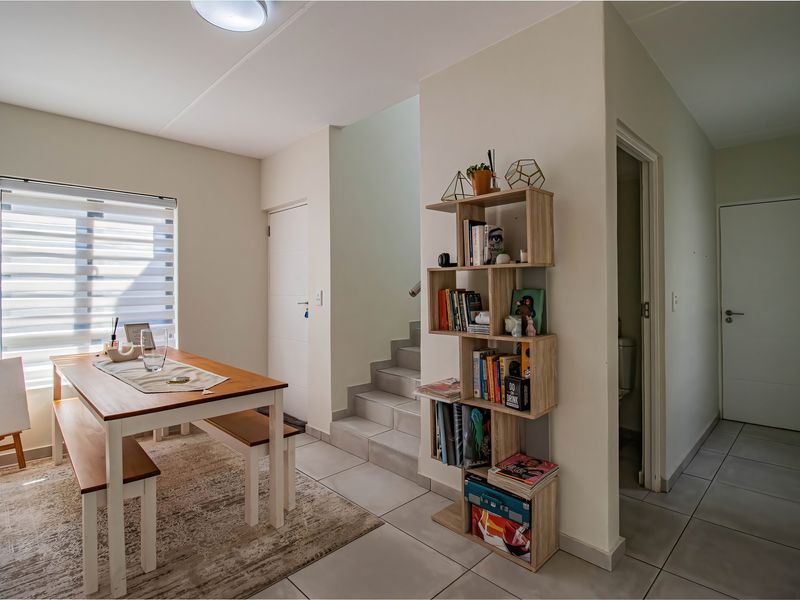 A bright dining area featuring tiled flooring, a staircase leading to the upper level, and modern zebra blinds on the window.