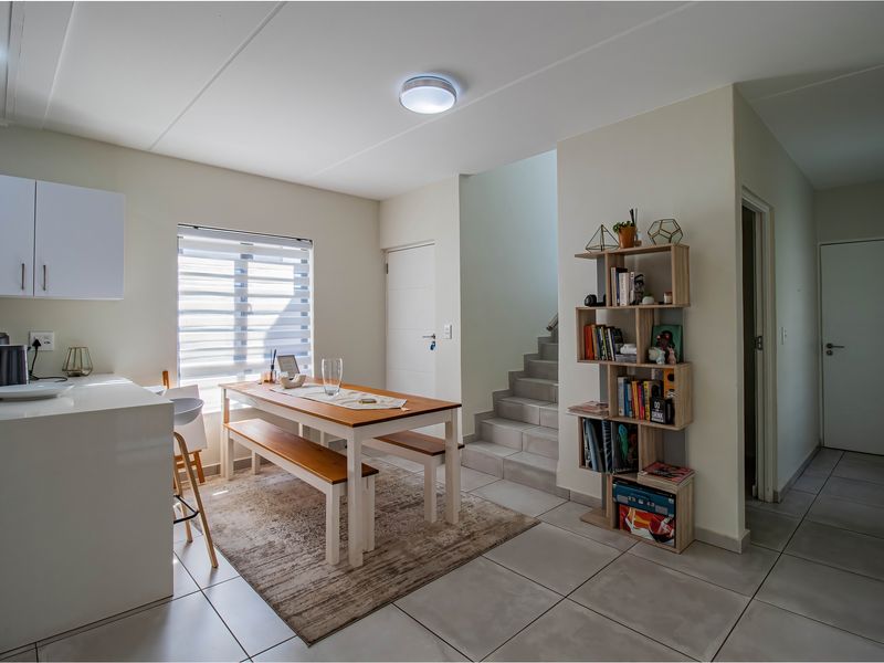 An open-plan living and dining area featuring tiled flooring, a staircase, and built-in kitchen cabinetry with neutral finishes.