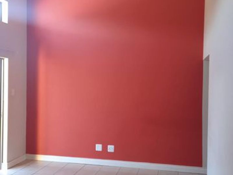 An empty living room featuring a high vaulted ceiling, ceramic tiled flooring, and a prominent red accent wall.