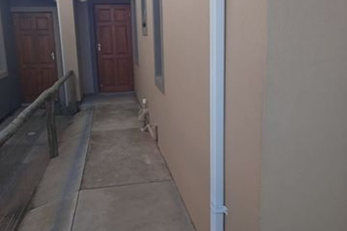 A side exterior walkway featuring concrete paving, a white downpipe, and access to two wooden exterior doors.
