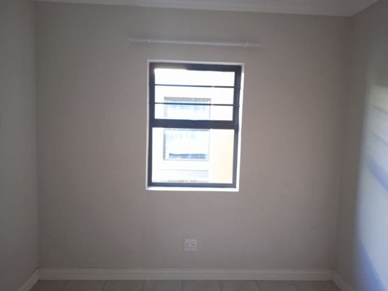 A clean, empty bedroom featuring neutral walls, tiled flooring, and a window fitted with security bars.
