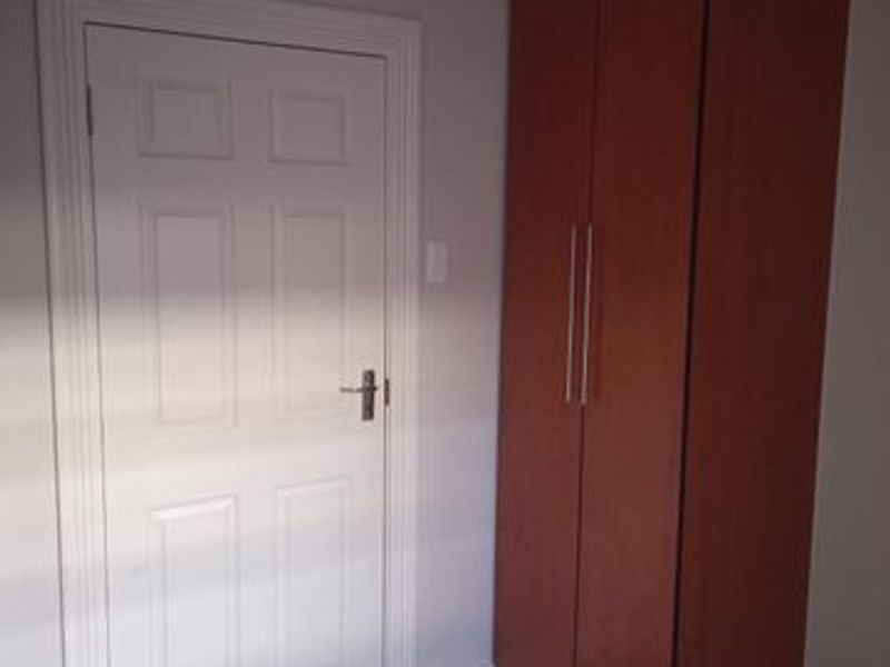 A clean bedroom interior featuring neutral wall tones, tiled flooring, and a tall built-in wooden cupboard.