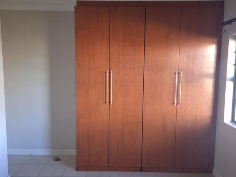 A bedroom featuring built-in wooden cupboards and tiled flooring, offering a clean and functional storage solution.