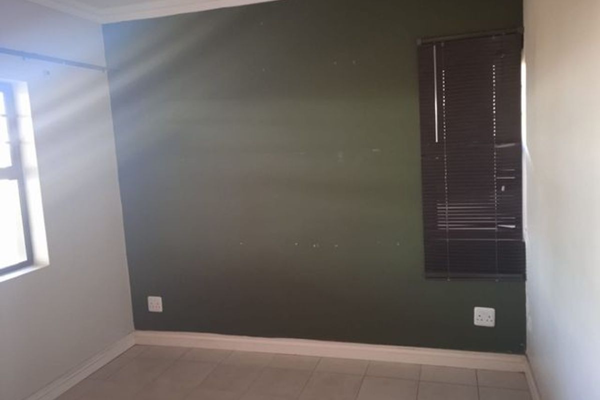 An empty bedroom featuring tiled flooring, a dark green accent wall with visible surface imperfections, and fitted venetian blinds.
