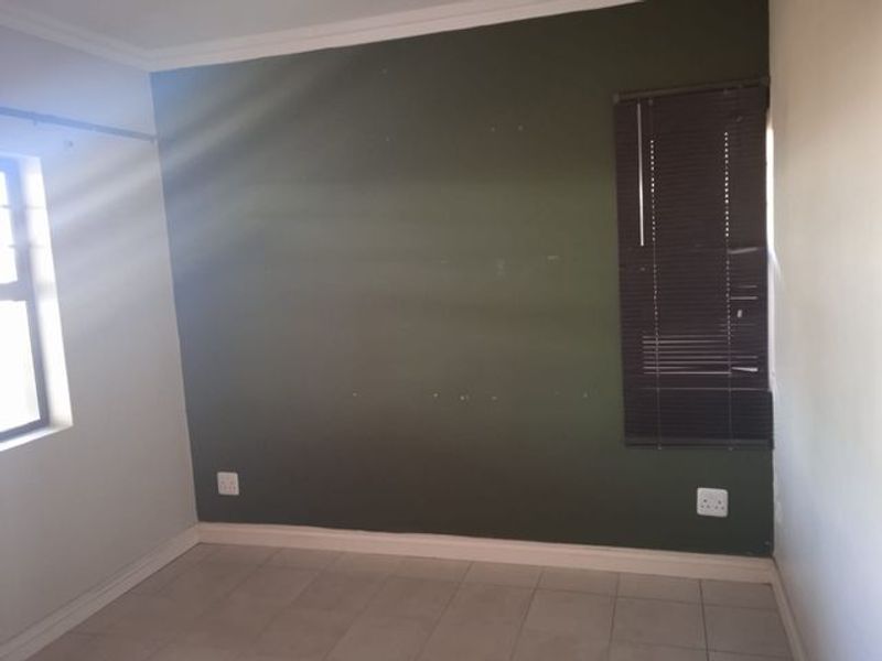 An empty bedroom featuring tiled flooring, a dark green accent wall with visible surface imperfections, and fitted venetian blinds.