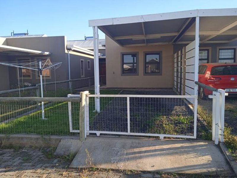 Front exterior view of the apartment featuring a covered carport, metal gate, and a gravel driveway with a small lawn area.