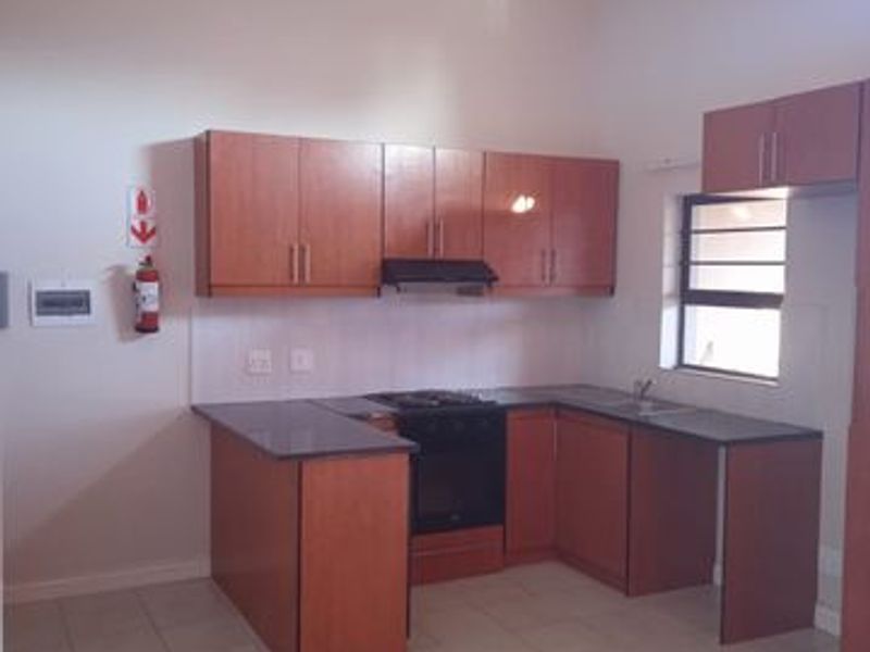 A functional kitchen featuring wooden cabinetry, granite countertops, built-in oven, hob, and extractor fan, set under a high vaulted ceiling with tiled flooring.