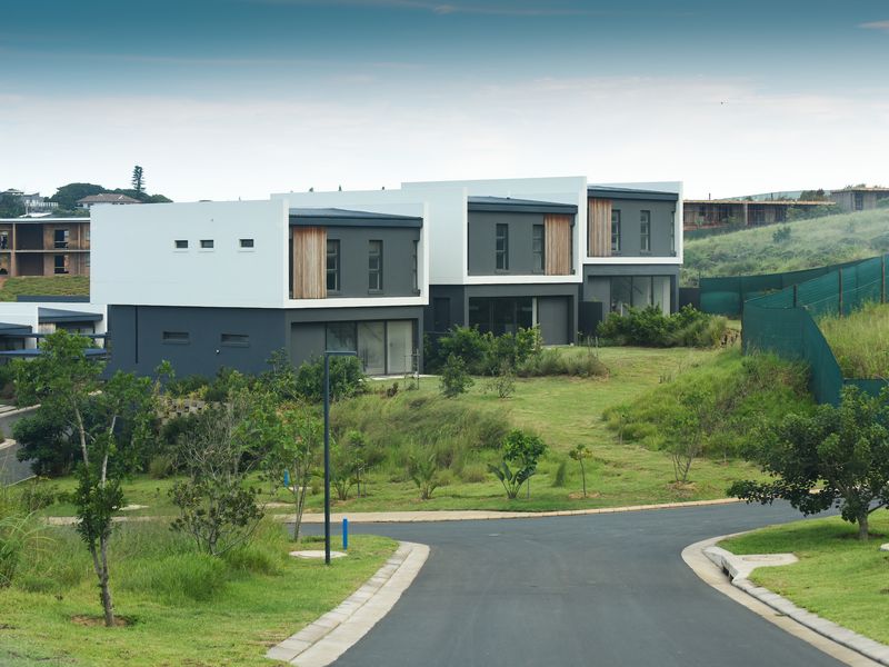 A view of modern residential townhouses featuring contemporary architectural design, set within a landscaped estate with paved access roads.