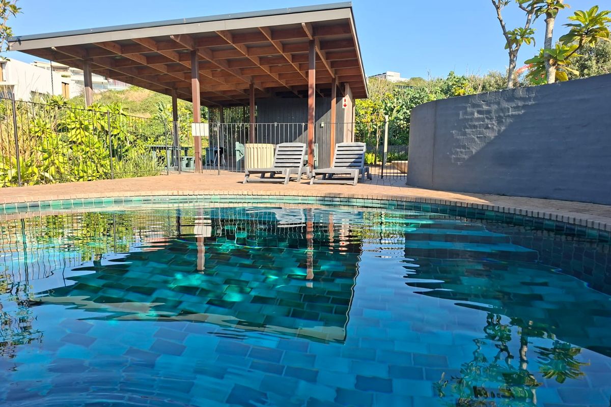 A well-maintained swimming pool area featuring a tiled pool, brick-paved surround, and a covered timber patio structure for outdoor relaxation.