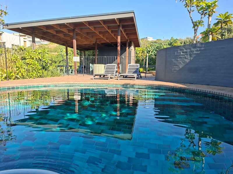 A well-maintained swimming pool area featuring a tiled pool, brick-paved surround, and a covered timber patio structure for outdoor relaxation.