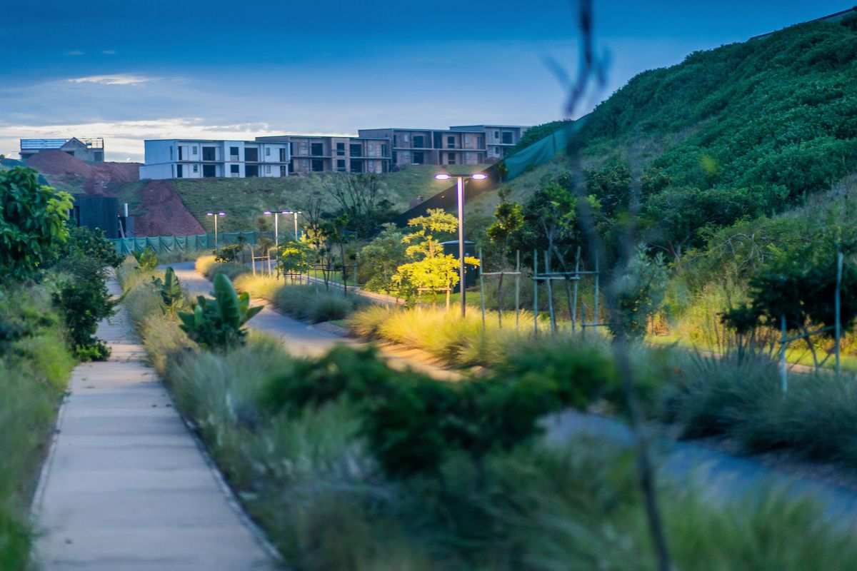 A view of a landscaped residential walkway and street lighting at dusk, with residential development visible in the background.