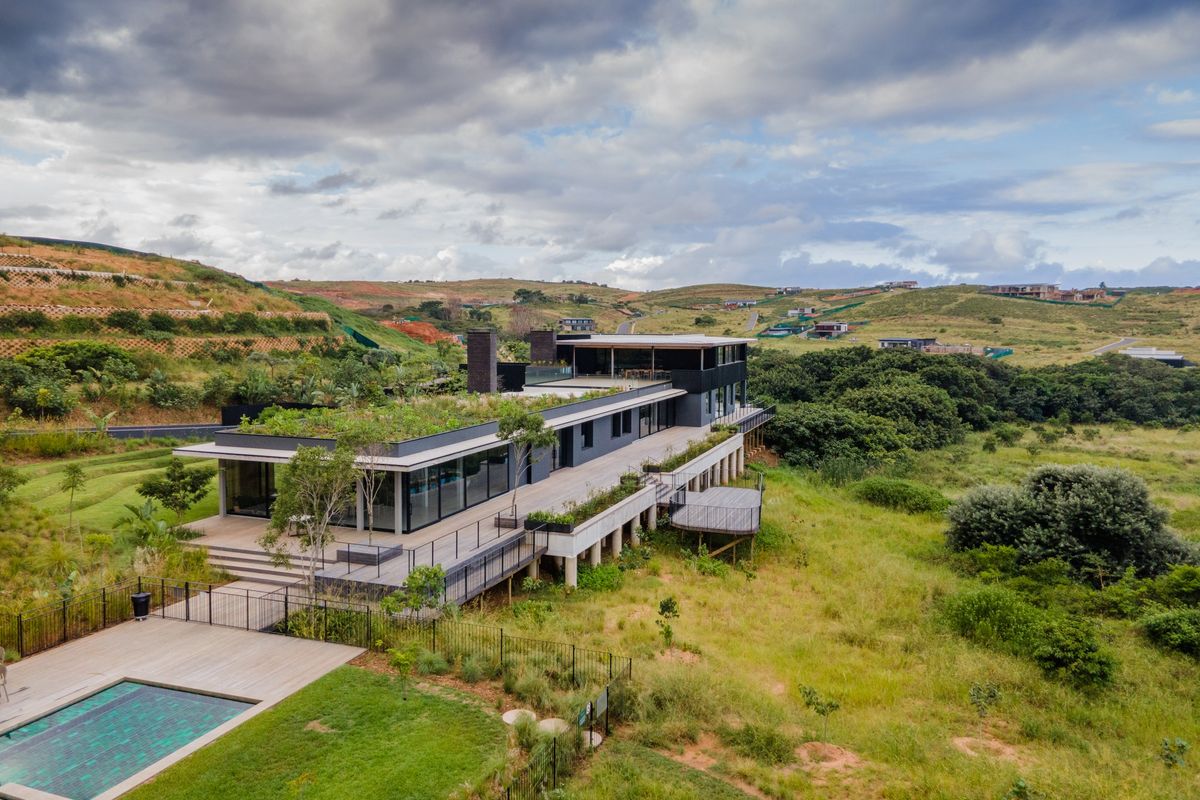 Aerial view of a modern architectural residence featuring a green roof, expansive timber decking, and a private swimming pool set in a landscaped estate.