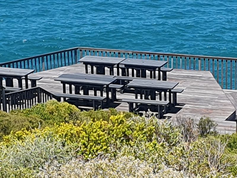 An elevated timber deck overlooking the ocean, featuring a wooden balustrade and open-air seating area.