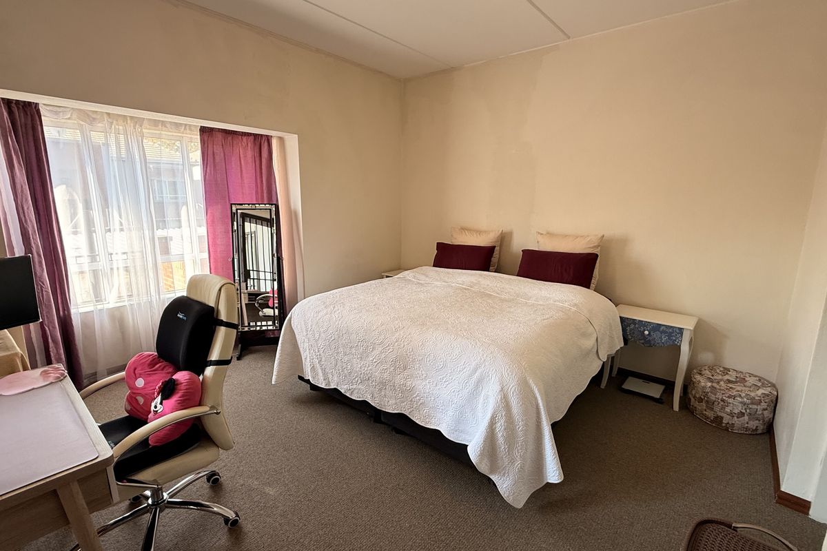 A spacious bedroom featuring carpeted flooring and a large window, providing natural light. The room requires minor cosmetic updates to the wall finishes.