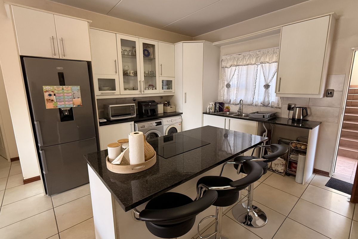 A functional kitchen featuring white cabinetry, dark granite countertops, a central island with a built-in hob, and ceramic tile flooring.