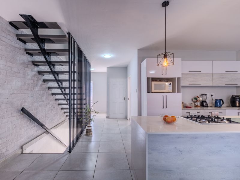 Modern open-plan kitchen featuring a central island with gas hob, sleek cabinetry, and a striking industrial-style staircase with a metal balustrade.