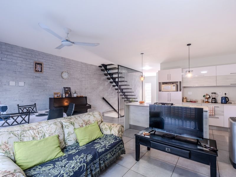 Open-plan living and kitchen area featuring an exposed brick wall, modern kitchen cabinetry, a central island, and a striking metal staircase.