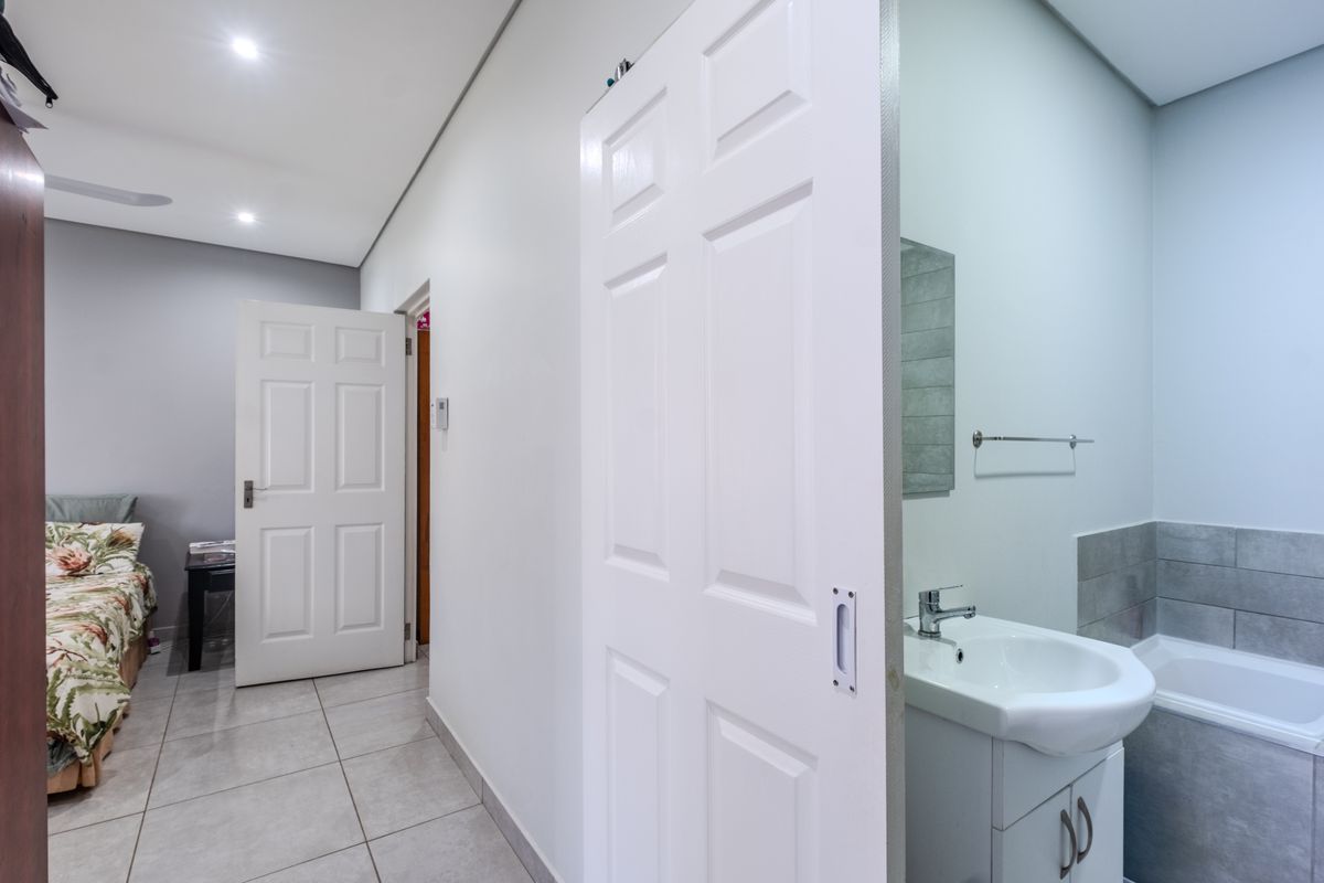 A clean, modern bathroom featuring a vanity basin with mixer tap, tiled splashback, and a bathtub, adjacent to a bedroom entrance.