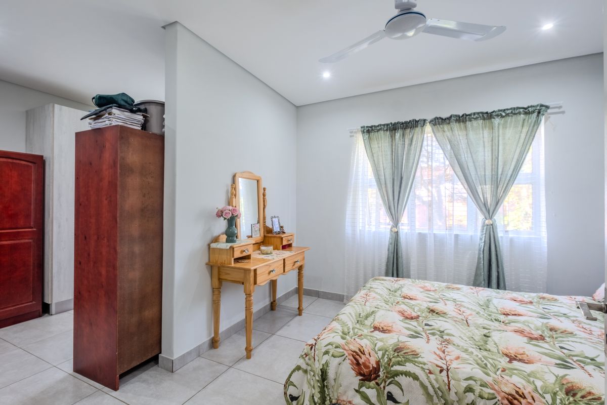 A well-lit bedroom featuring neutral tiled flooring, a ceiling fan, and a built-in cupboard, offering a clean and functional living space.