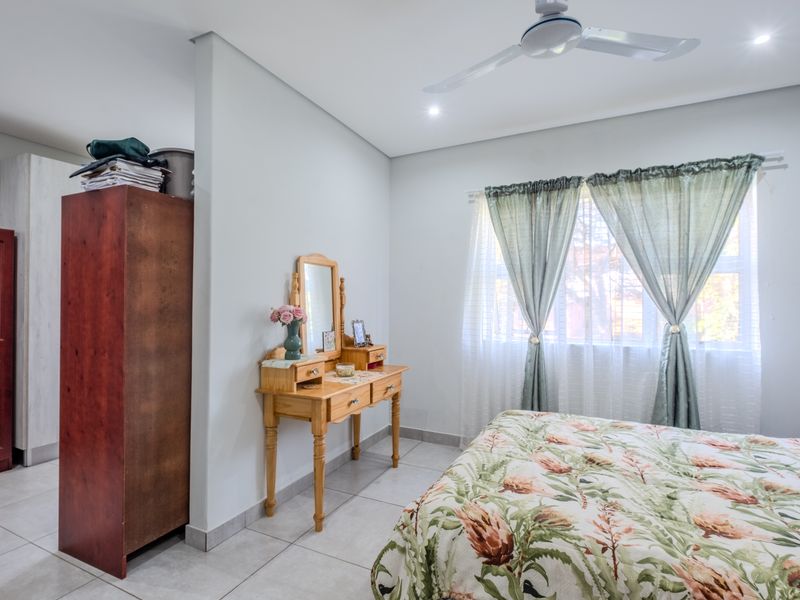 A well-lit bedroom featuring neutral tiled flooring, a ceiling fan, and a built-in cupboard, offering a clean and functional living space.