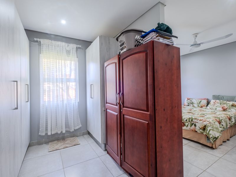 Spacious bedroom featuring extensive built-in cupboard storage, tiled flooring, a ceiling fan, and neutral wall finishes.