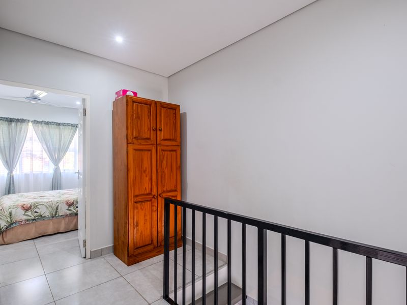 A bright upstairs landing area featuring tiled flooring, a modern metal balustrade, and recessed lighting, providing access to an adjacent bedroom.