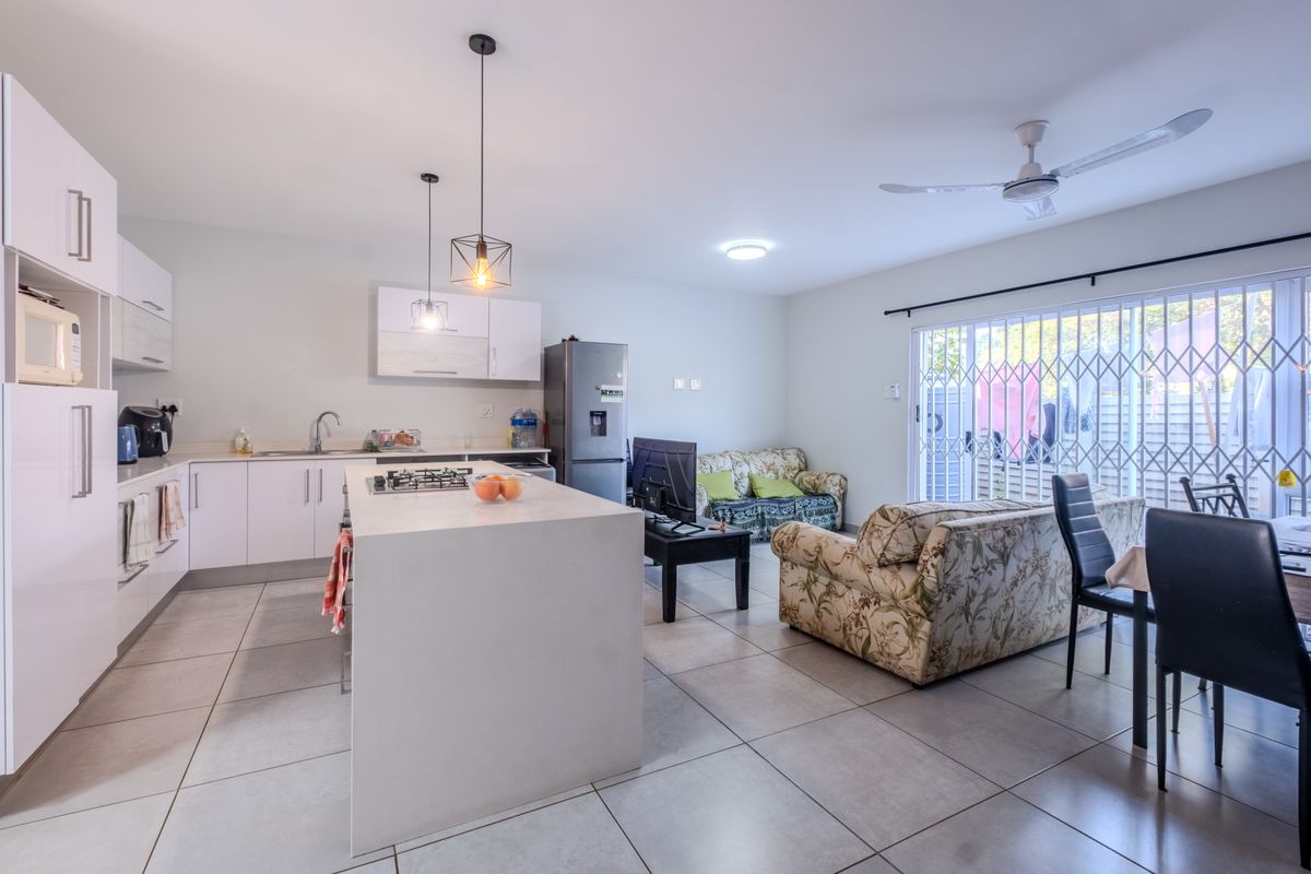 Modern open-plan living area featuring a sleek kitchen with a central island, gas hob, and direct access to the outdoor patio through sliding doors.