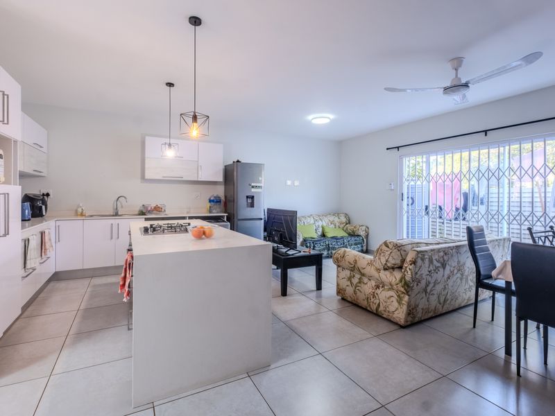Modern open-plan living area featuring a sleek kitchen with a central island, gas hob, and direct access to the outdoor patio through sliding doors.
