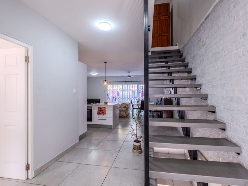 Open-plan living area featuring a modern open-tread staircase, exposed brick feature wall, and a functional kitchen island with built-in oven.