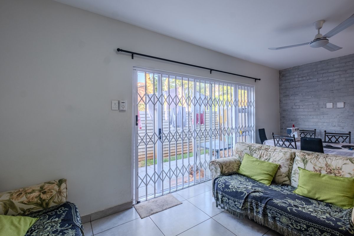 Living area featuring tiled floors, a ceiling fan, and an exposed brick wall, with direct access to the rear patio through a sliding glass door.